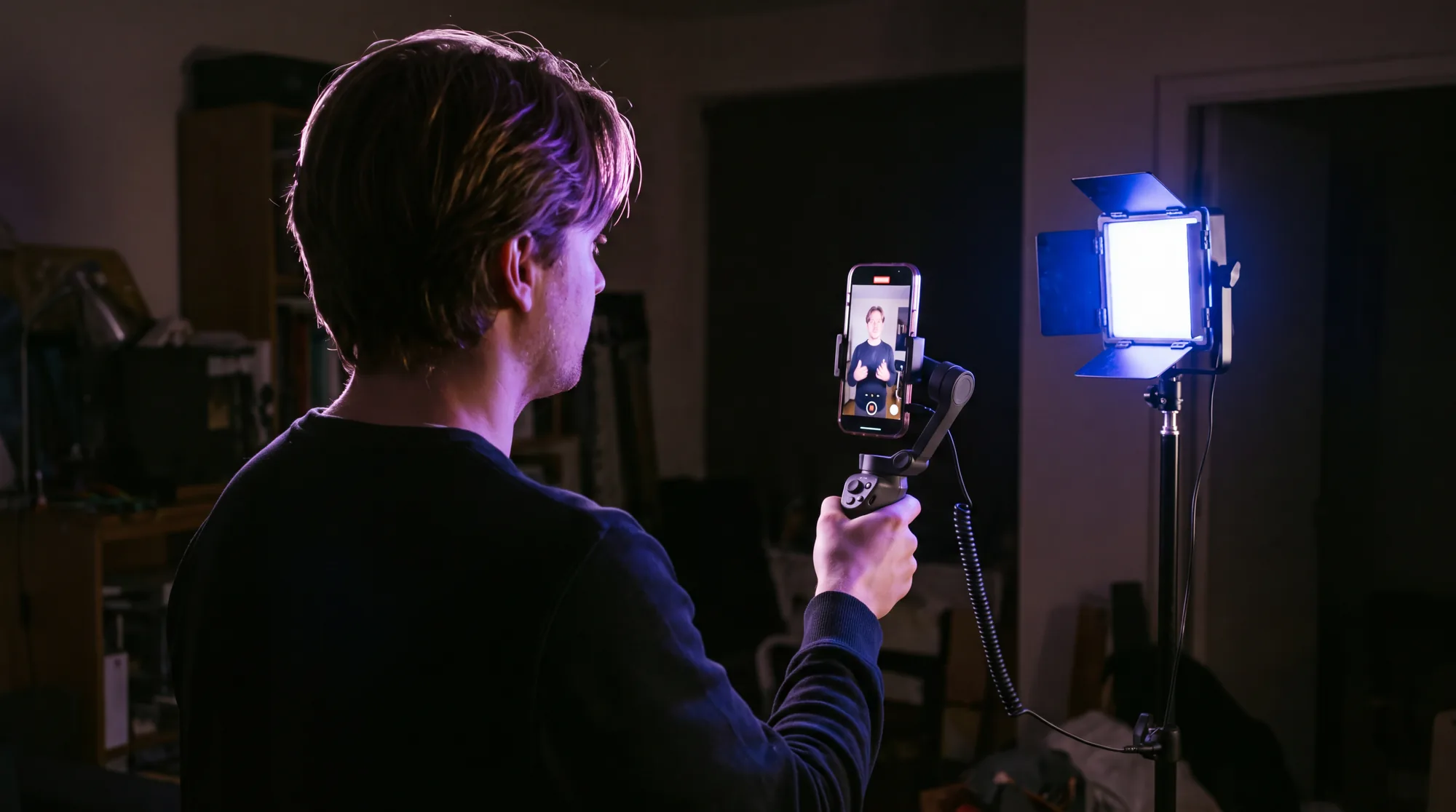 Ein Mann filmt von hinten gesehen mit einem hochkant eingespannten Telefon auf einem Gimbal, daneben leuchtet ein LED-Flächenlicht